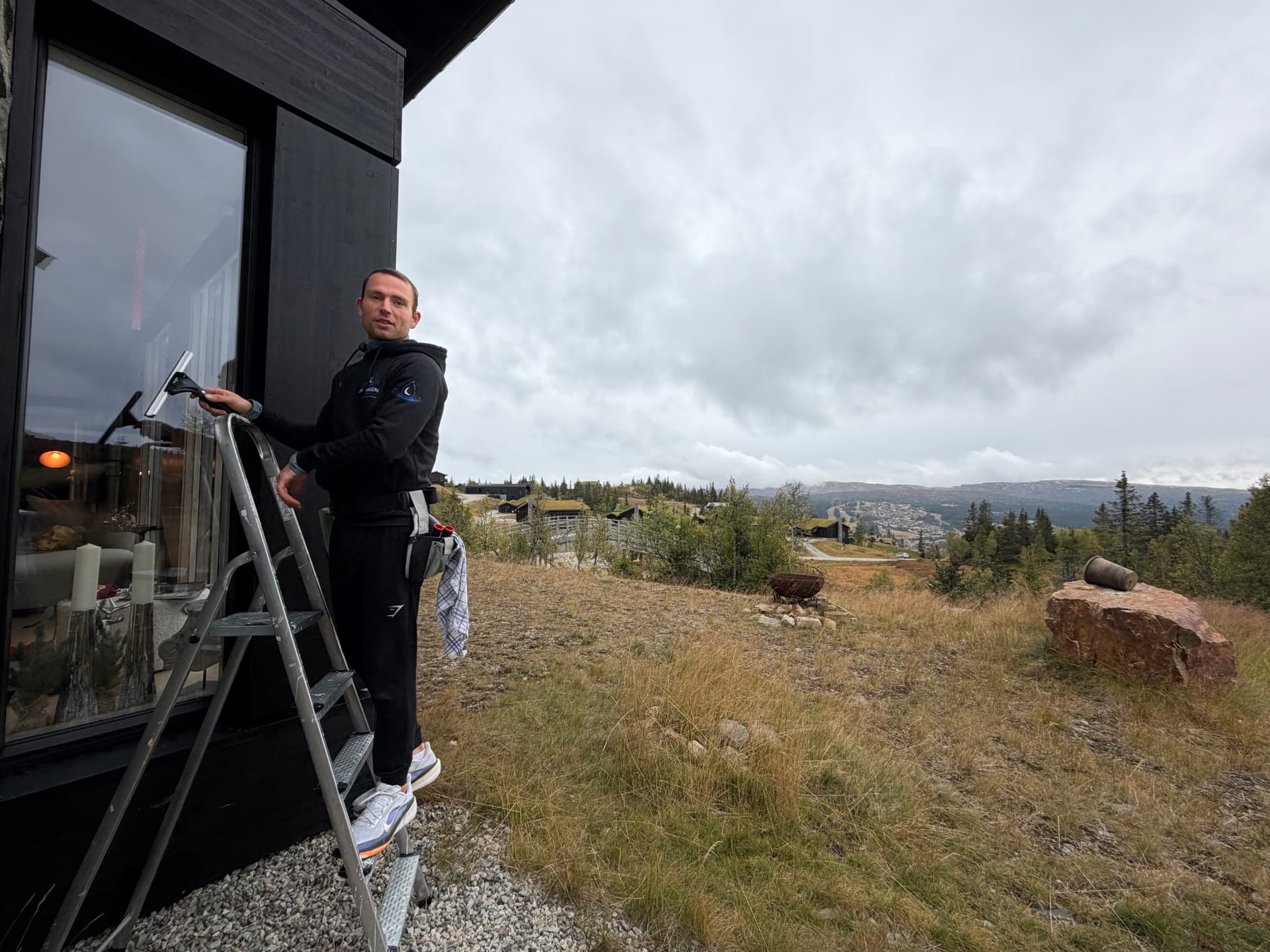 Johan Hansen vasker et stort hyttevindu med nal fra en stige